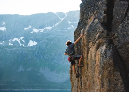 A horizontal shot of a person climbing the rocky hill with beautiful snowy mountains in the background